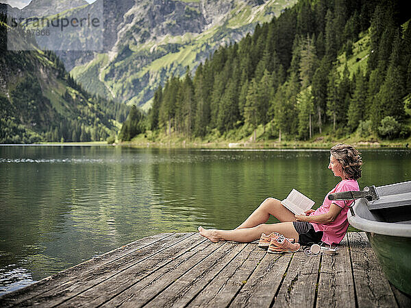 Frau liest Buch mit dem Ruderboot am See