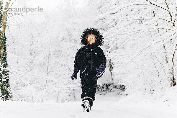 Lächelndes Mädchen  das auf schneebedecktem Land im Winterwald spaziert