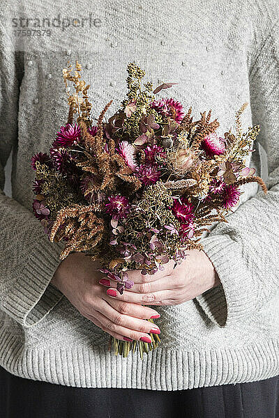 Mid section of woman holding bouquet of various dried flowers