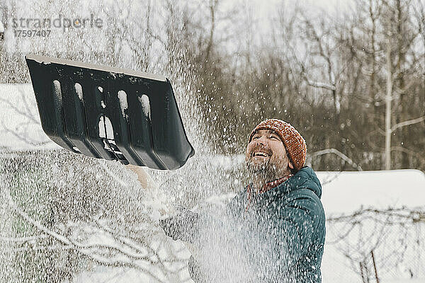 Verspielter Mann wirft im Winter Schnee von der Schneeschaufel