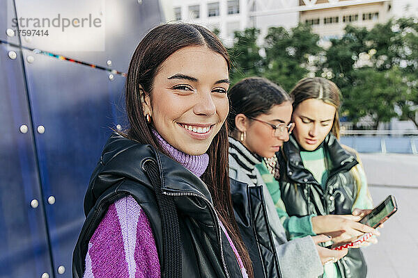 Smiling young woman standing by friends using smart phone