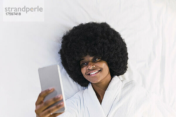 Lächelnde Frau  die zu Hause im Bett liegt und ihr Smartphone benutzt