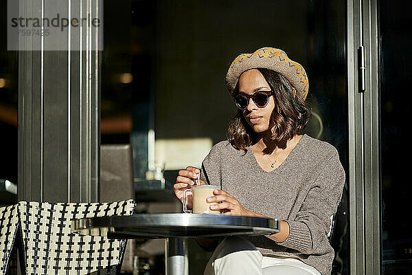 Junge Frau rührt an einem sonnigen Tag Kaffee im Café