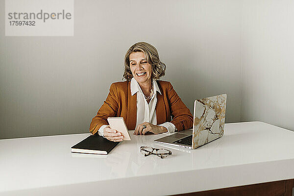 Glückliche Geschäftsfrau  die am Schreibtisch mit ihrem Smartphone im Internet surft
