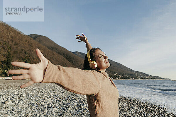 Lächelnde junge Frau  die über Kopfhörer Musik hört und am Strand tanzt