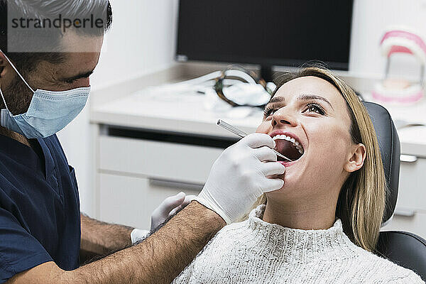 Zahnarzt analysiert während COVID-19 die Zähne des Patienten im Behandlungsraum der Klinik
