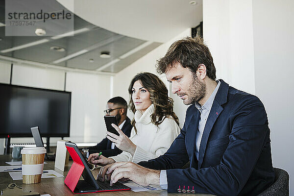 Geschäftsfrau arbeitet am Laptop und sitzt neben Kollegen am Schreibtisch im Büro