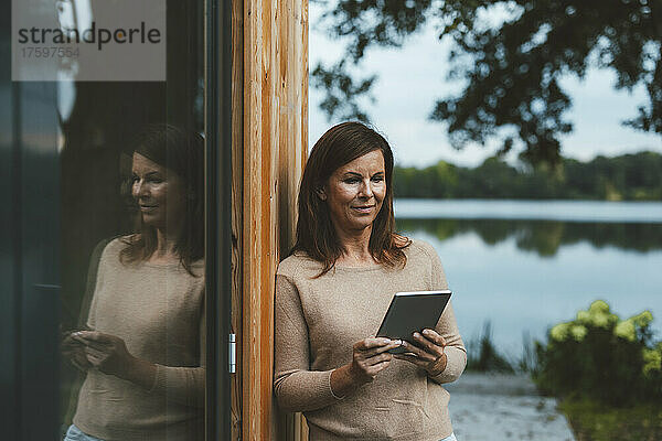 Frau mit braunen Haaren benutzt Tablet-PC vor Glaswand im Hinterhof