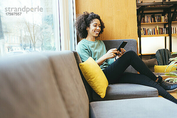 Lächelnde Geschäftsfrau benutzt Smartphone auf dem Sofa
