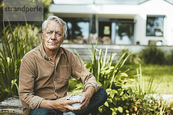 Nachdenklicher älterer Mann mit Kaffeetasse sitzt im Garten