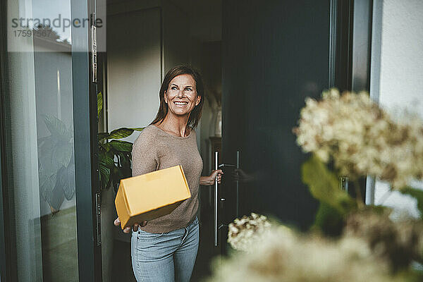 Glückliche Frau mit Paket steht vor der Tür