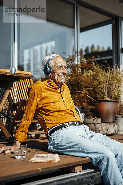 Lächelnder älterer Mann  der an einem sonnigen Tag auf dem Hausboot Musik über drahtlose Kopfhörer hört