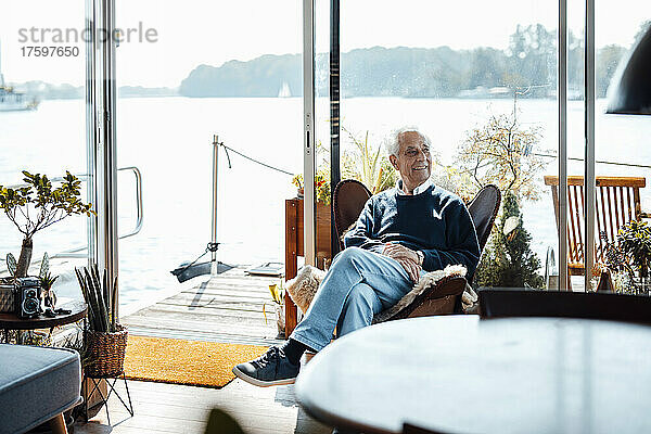 Lächelnder älterer Mann sitzt auf einem Stuhl am Hausboot