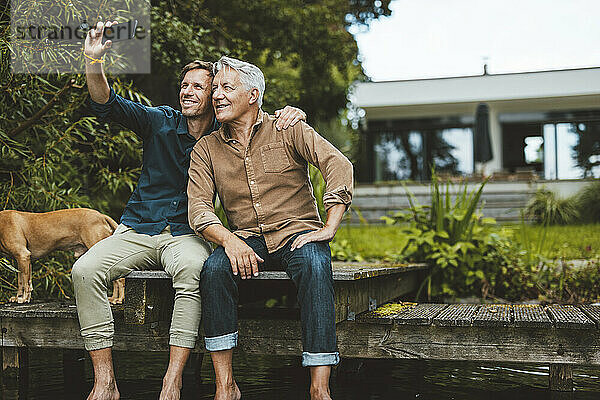 Lächelnder Mann macht mit seinem Vater im Hinterhof ein Selfie per Smartphone