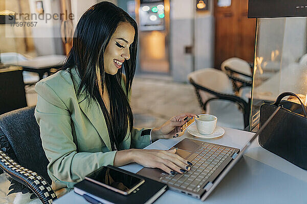 Lächelnder Freiberufler beim Online-Shopping am Laptop im Café