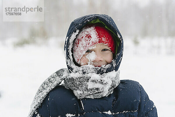Glücklicher Junge mit Schnee auf Schal im Wald