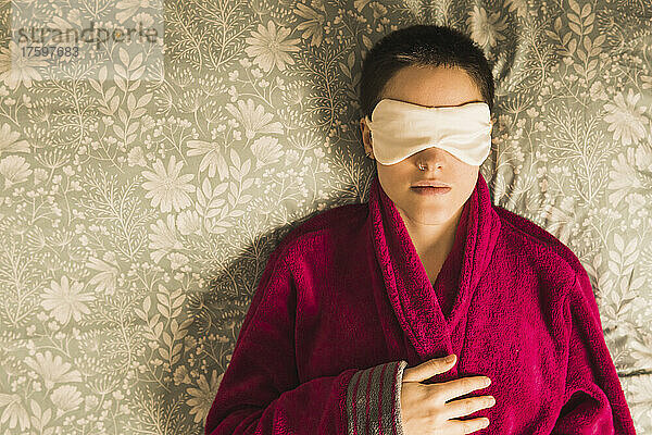 Woman wearing eye mask relaxing on bed at home