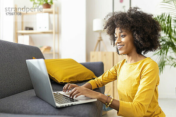 Glückliche junge Frau  die zu Hause einen Laptop neben dem Sofa benutzt