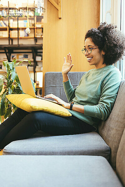 Smiling businesswoman waving on video call through laptop on sofa