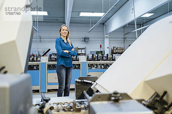 Smiling businesswoman standing with arms crossed in factory