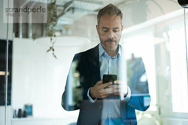 Geschäftsmann benutzt Smartphone  gesehen durch Glasfenster im Büro