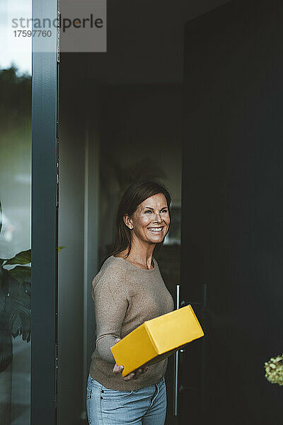 Glückliche Frau mit gelbem Paket steht vor der Haustür