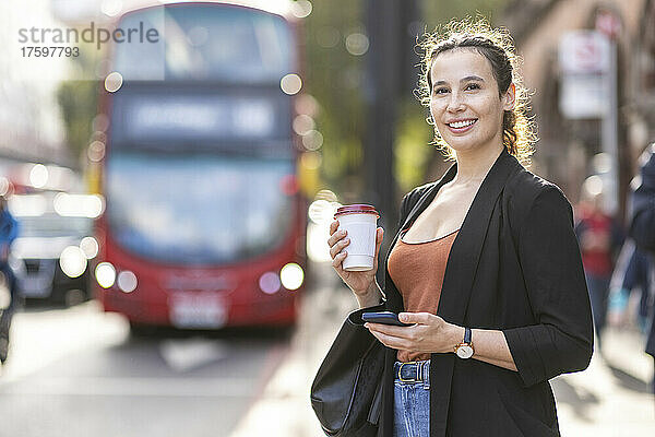 Lächelnde Geschäftsfrau mit Einwegkaffeetasse unterwegs in der Stadt