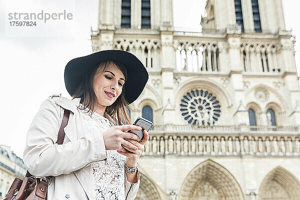 Junge Frau benutzt Mobiltelefon an der Kathedrale Notre Dame