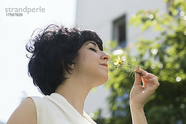 Frau mit geschlossenen Augen duftet an einem sonnigen Tag nach gelber Blume