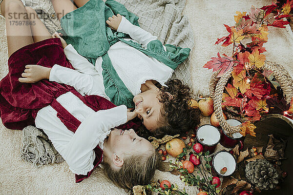 Smiling girls lying on blanket by fruits at picnic in forest