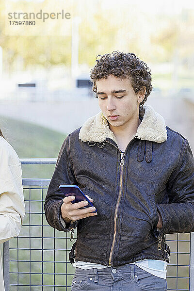 Junger Mann benutzt Smartphone vor Geländer