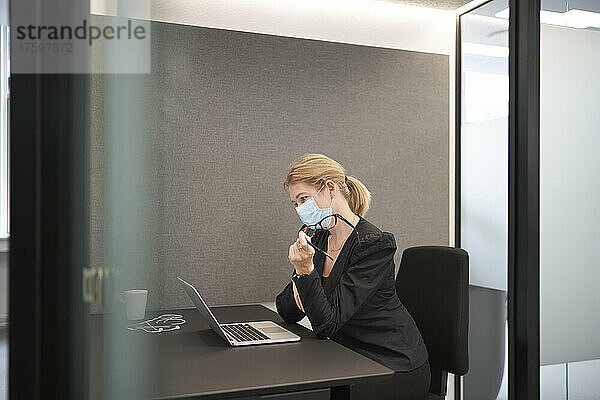 Geschäftsfrau mit Gesichtsmaske arbeitet am Laptop am Schreibtisch