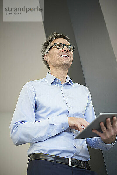 Lächelnder Geschäftsmann mit Tablet-PC  der im Büro träumt