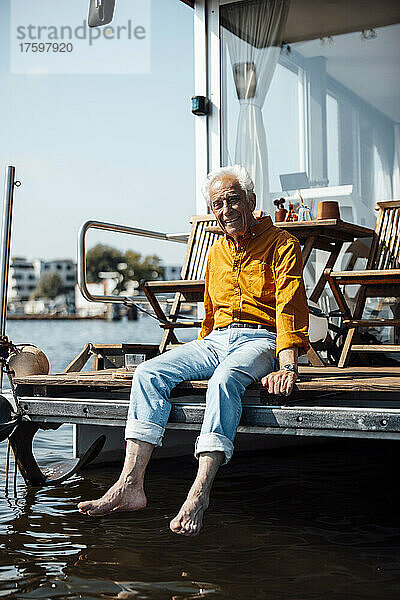 Lächelnder älterer Mann sitzt an einem sonnigen Tag am Hausboot