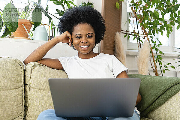 Lächelnder Freiberufler mit Laptop auf Sofa zu Hause