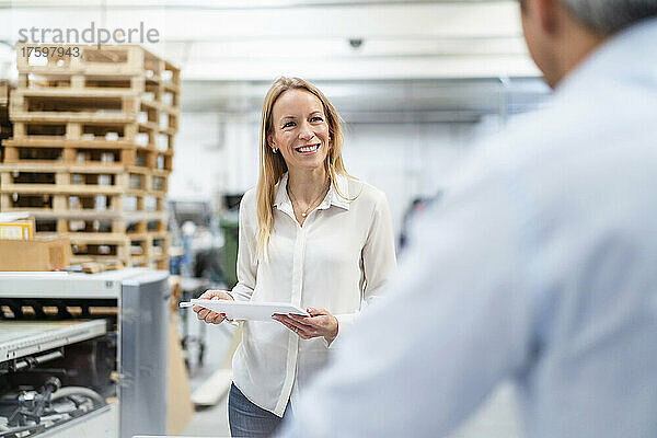 Lächelnde Geschäftsfrau mit Tablet-PC blickt auf Kollegen in der Industrie