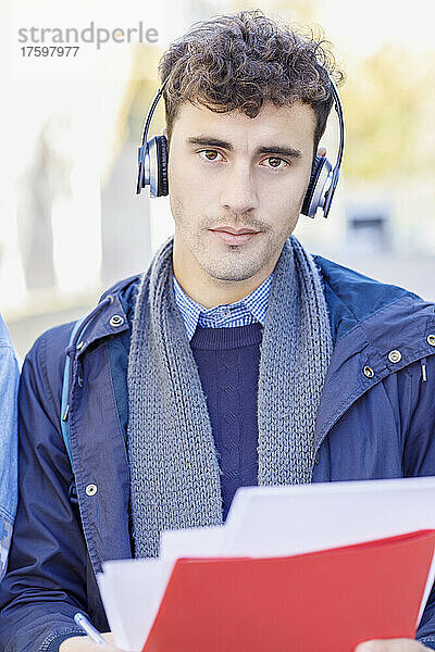 Junger Mann hört Musik über Kopfhörer auf dem Universitätscampus