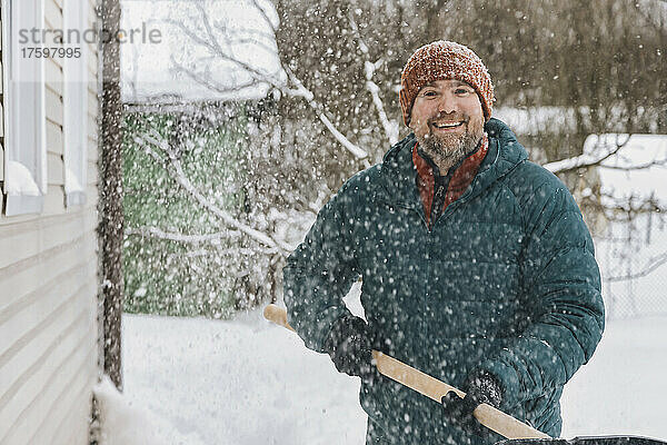 Mann mit Schneeschaufel steht im verschneiten Garten