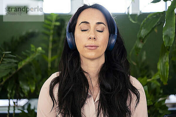 Geschäftsfrau mit geschlossenen Augen hört Musik über Kopfhörer im Coworking-Büro