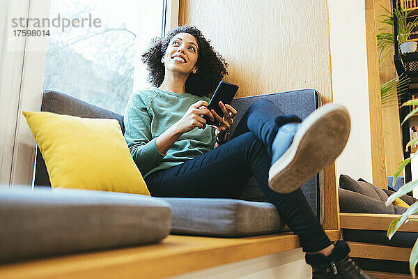 Nachdenkliche Geschäftsfrau mit Smartphone auf dem Sofa