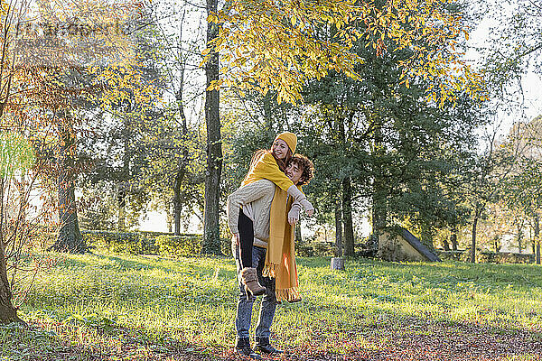 Junger Mann gibt seiner Freundin Huckepackfahrt im Herbstpark