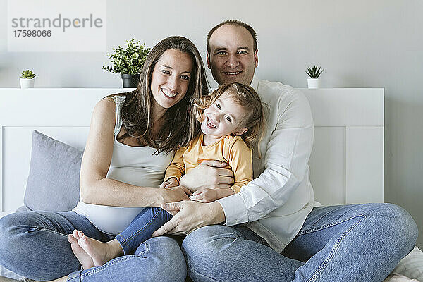 Happy man and woman with daughter sitting on bed at home