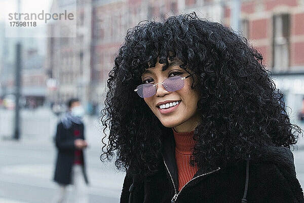 Lächelnde junge Frau mit lockigem schwarzem Haar und Sonnenbrille