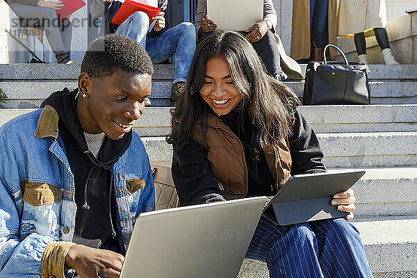 Lächelnde Frau lernt mit Freundin über Laptop auf dem Campus