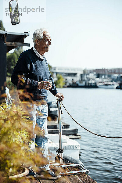 Älterer Mann mit Trinkglas am Hausboot an einem sonnigen Tag