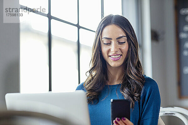 Lächelnde Geschäftsfrau benutzt Mobiltelefon im Café