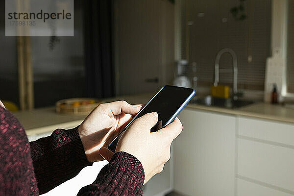 Frau benutzt Smartphone an sonnigem Tag in der Küche