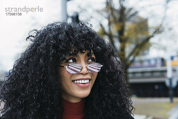 Straßenmarkierung reflektiert die Sonnenbrille einer lächelnden jungen Frau mit lockigem schwarzem Haar