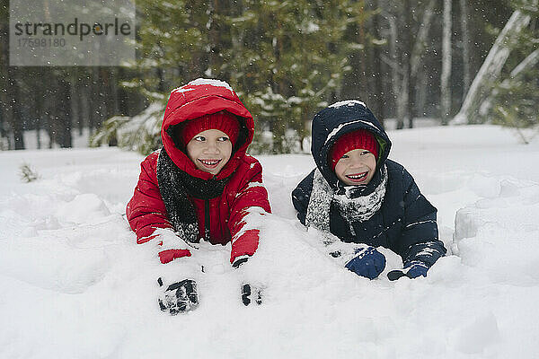 Verspielte Zwillingsbrüder liegen im Winter auf Schnee