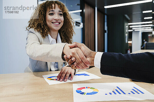 Lächelnde Geschäftsfrau schüttelt einem Kollegen im Coworking-Büro die Hand